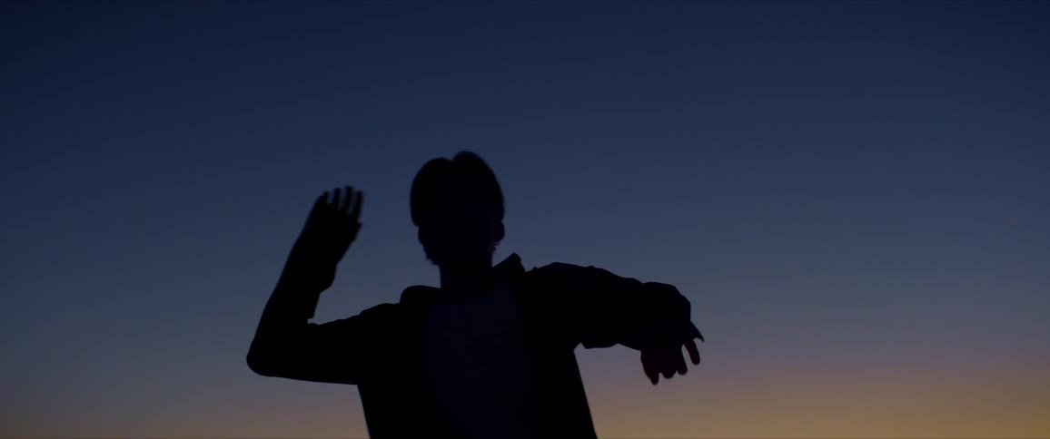Silhouette of a man moving his arms while dancing against a morning sky