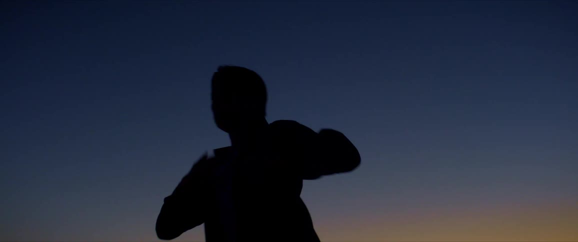 A male dancer is silhouetted against the sunset while dancing