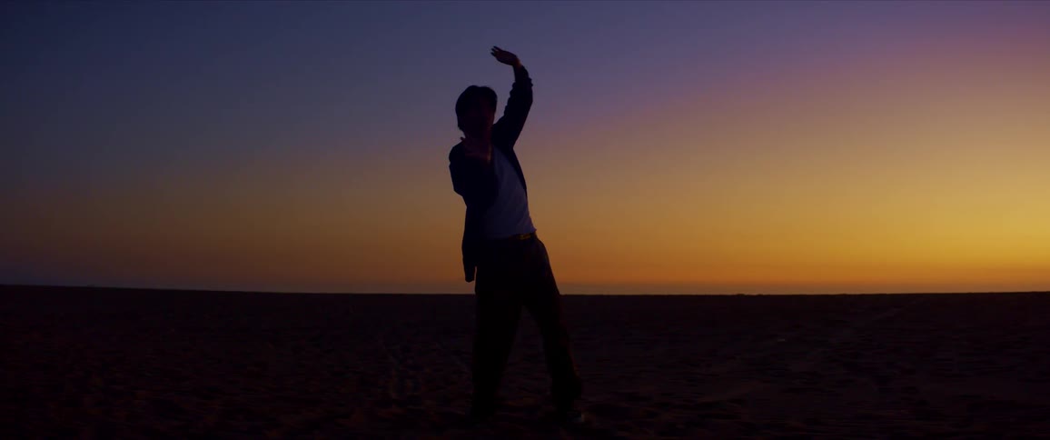 Silhouette of a man standing on the beach sand dancing against a reddish sky