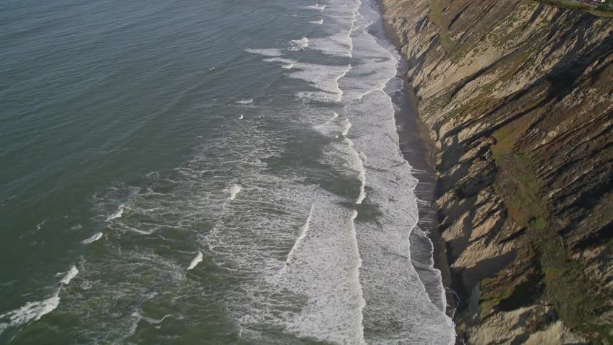 Aerial panorama of rocky mountains at the edge of an ocean with foamy waves