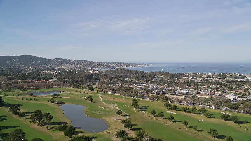 Aerial view of a golf course and the suburban coastal town beyond it
