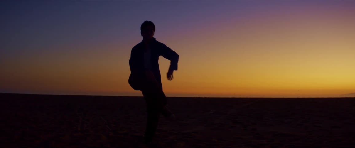 Silhouette of a man dancing on the beach sand against a reddish sky