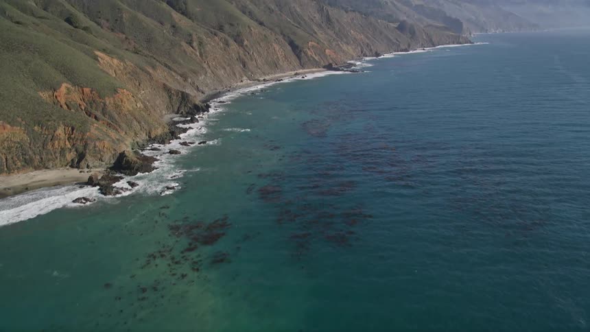 Waves flow past seaside mountains on a foggy day