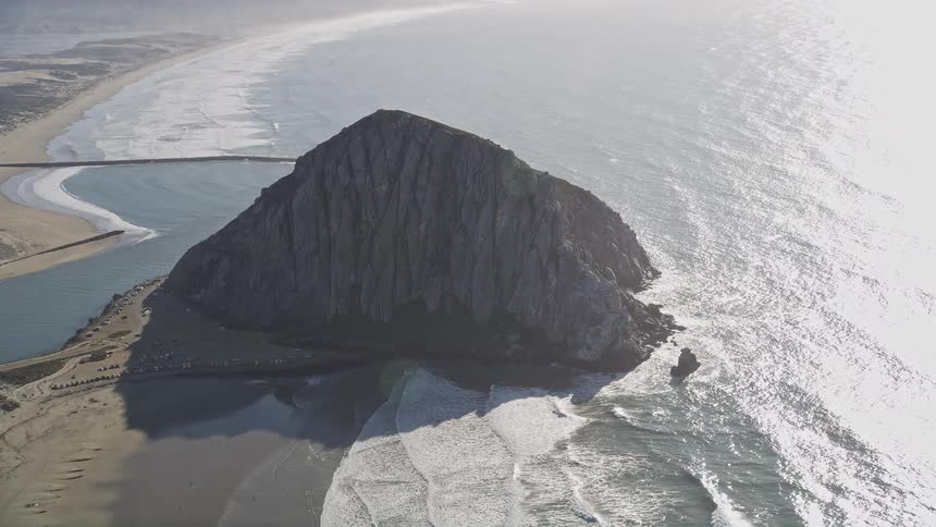 Aerial landscape of a large mountain with a cliff surrounded by sand and an extensive sea