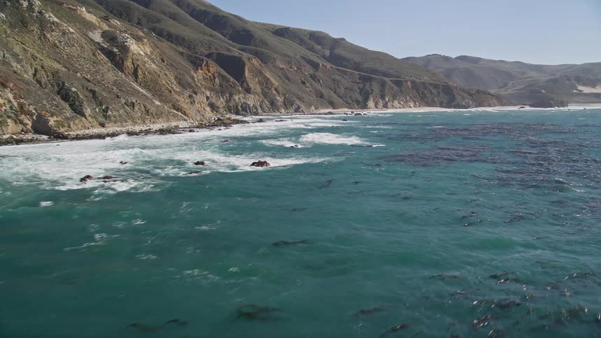 Blue ocean with algae on the edge of the mountainous coast