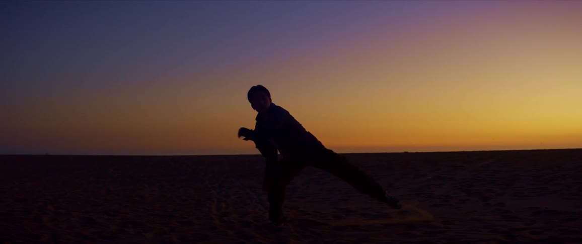 Red sky and the silhouette of a person dancing on the beach sand