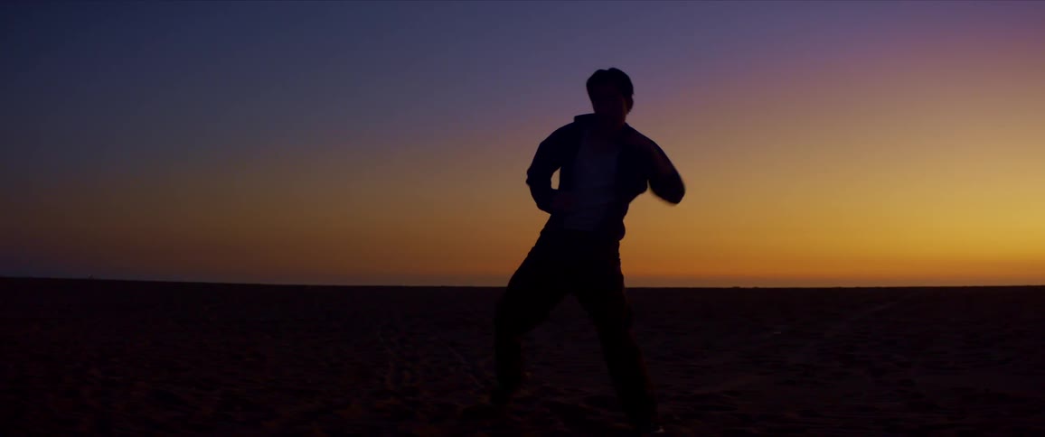 Silhouette of a person dancing against the sky colored by the sunset