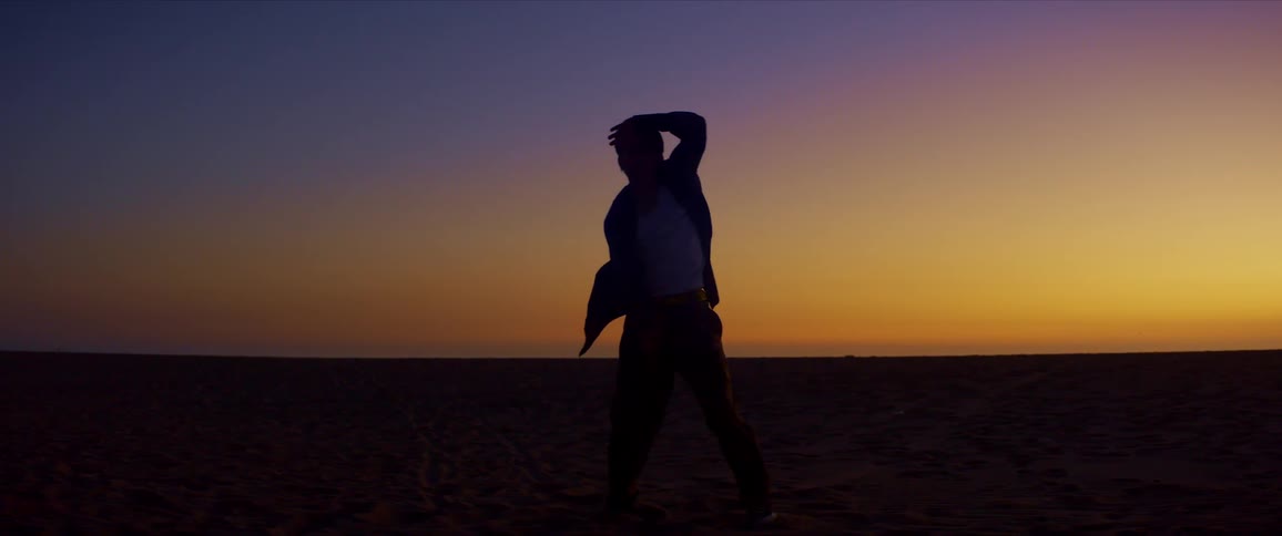 A male dancer is silhouetted against the sunset while dancing