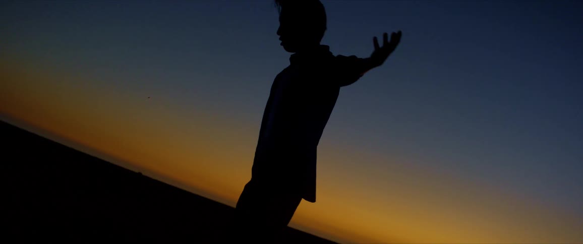 Silhouette of a man moving his arms and legs dancing against a blue and yellowish sky