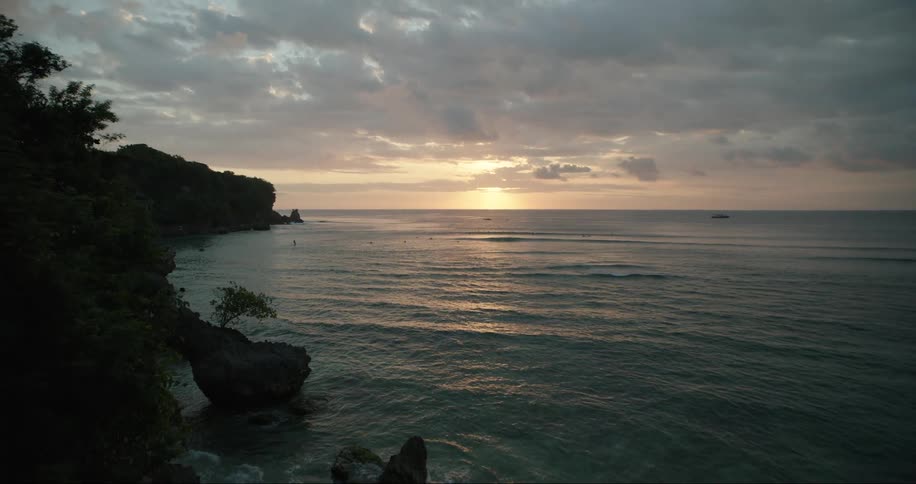 Person opens window while sun sits on pale pink horizon over the ocean
