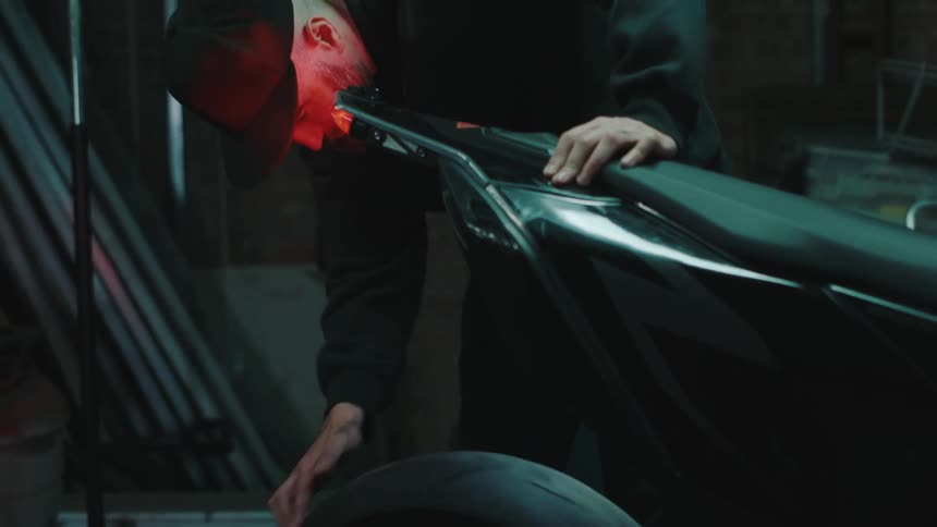 Mechanic with a beard and cap turning the rear wheel of a motorcycle