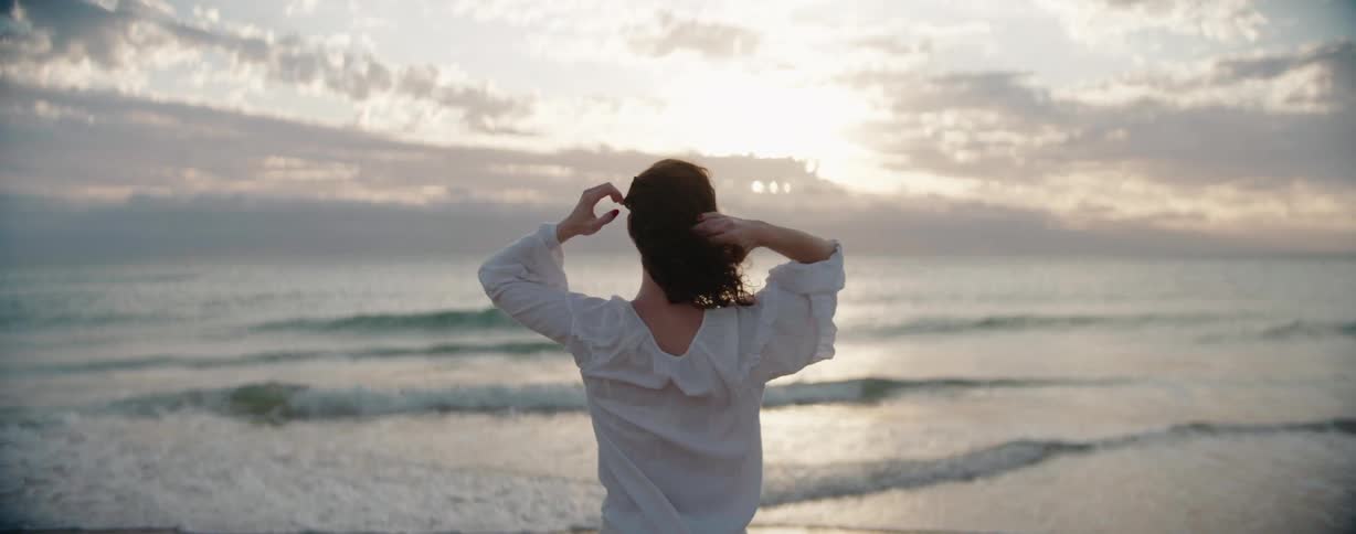 A woman raises her arms on the beach