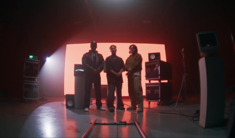 Three male models side by side inside a studio with vintage equipment on a lit screen in the background