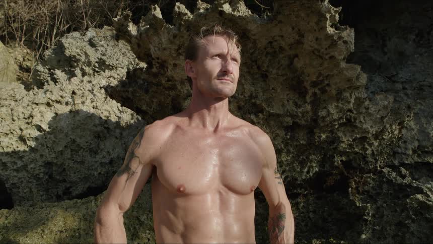 Man without a shirt next to a rock in a natural environment