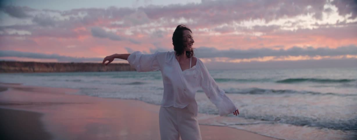 A young woman stands on the beach and waves her arms at sunset