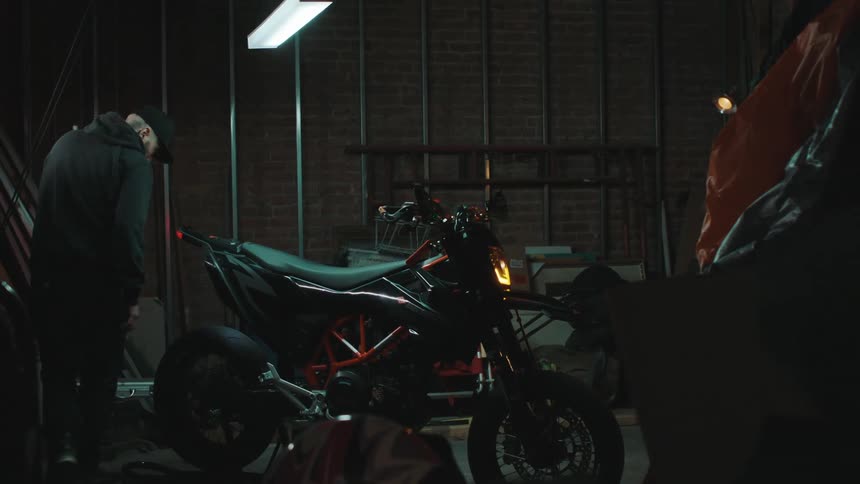 A moment in a black coat and cap is working on a motorcycle that is stopped and flashing its warning lights