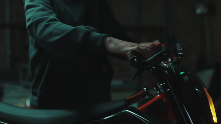 Male mechanic examines motorcycle while standing in a dimly lit garage