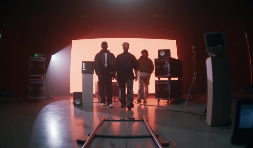 Three male models walking side by side in a dimly lit studio with a red screen in the background