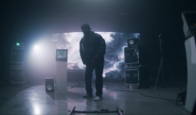 A musician walks forward and squats down into a pose on a music video stage