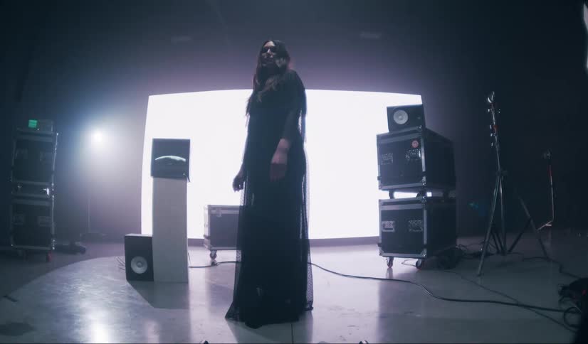 Model woman modeling in a long black dress in a dimly lit studio with a glowing screen in the background