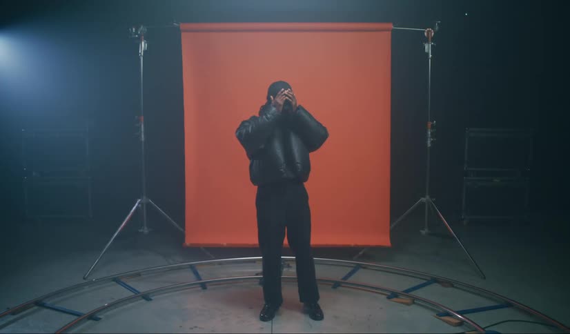 A stands in front of an orange backdrop surrounded by studio equipmen