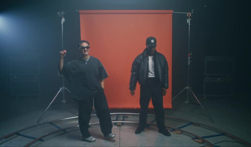 Two men are in a studio and they shake hands and behind there is an orange background
