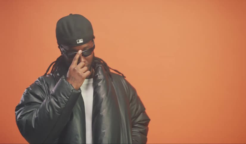 Portrait of a model man putting his hand on his sunglasses while standing in a studio with an orange background