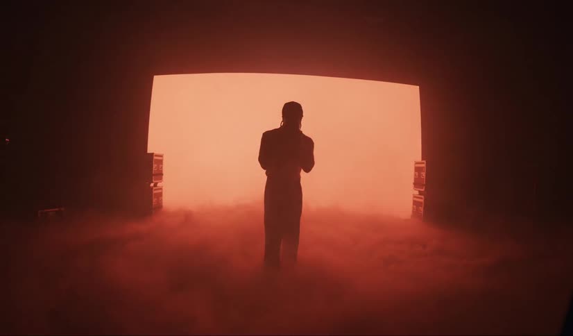 A silhouette of a man shadow boxing in front of a brightly lit screen surrounded by smoke