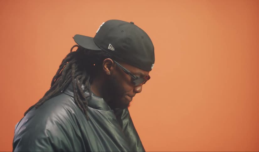 Portrait of a man with sunglasses and a backwards cap parading in a studio with an orange banner in the background