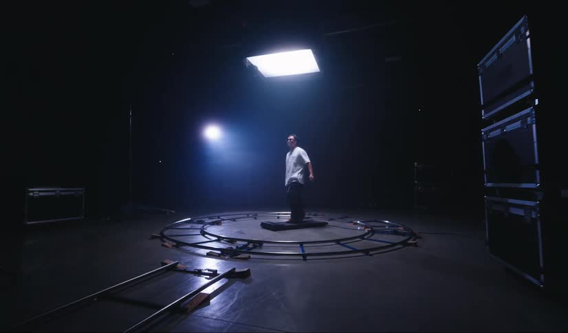 A man is walking on a treadmill which is between a circular shape in a dark studio with a light on top of him