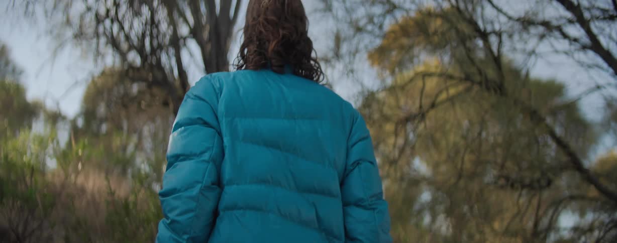 Back view of a woman in a blue jacket walking in a natural environment with trees around
