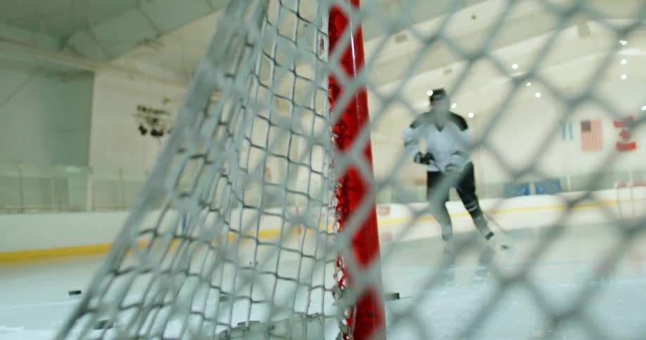 Hockey players skating near a goal on an indoors ice rink