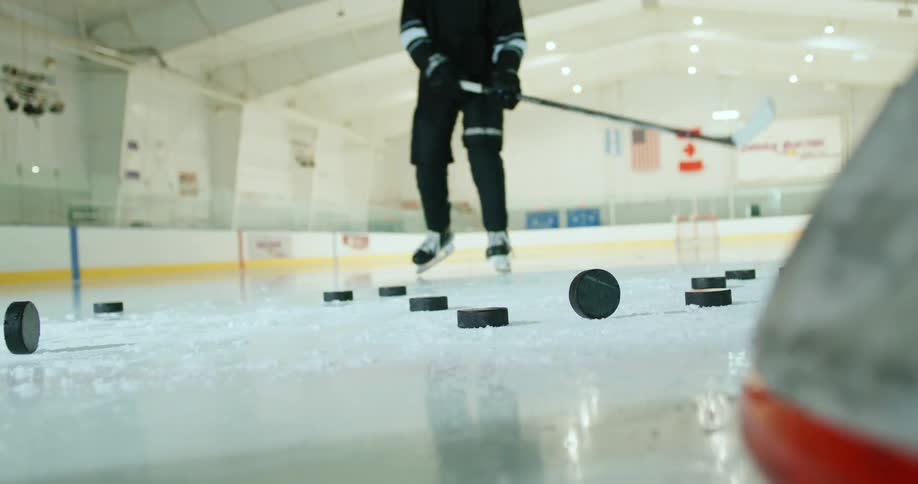 A player skating on an indoor ice hockey rink with scattered black pucks on the surface