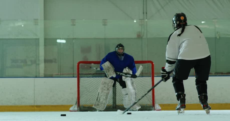 Hockey player moves puck across the ice and takes a shot that the goalie blocks