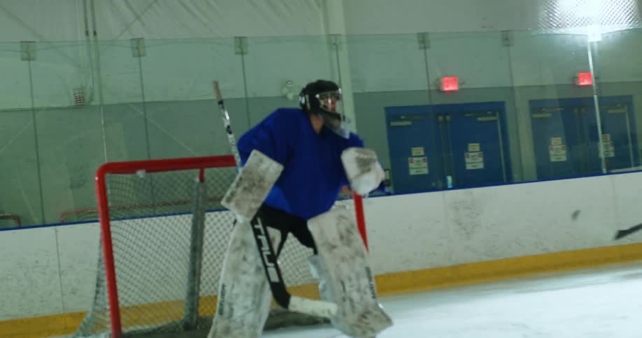 Player throwing a hockey puck towards the goal and scoring the goalkeeper on an ice court