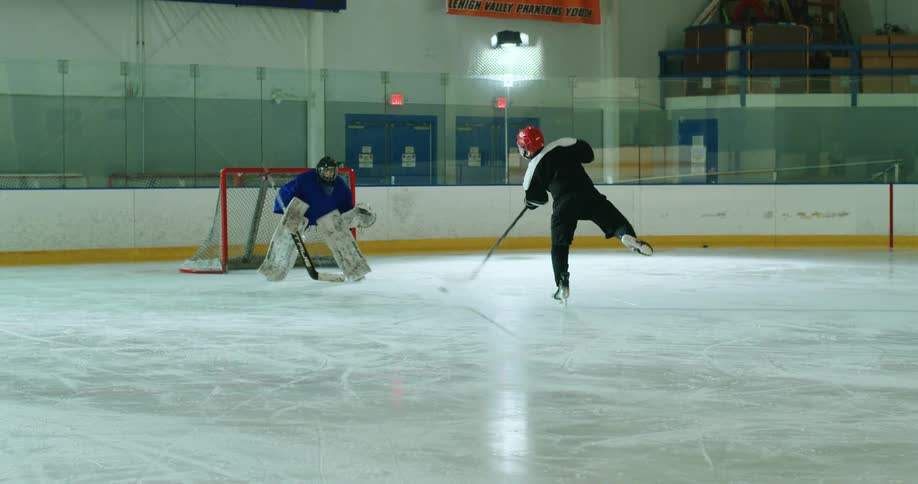 Player throwing a puck towards the goal with his hockey stick