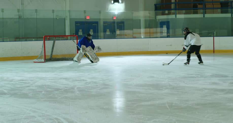 A player takes a shot at a goalie on an ice hockey rink