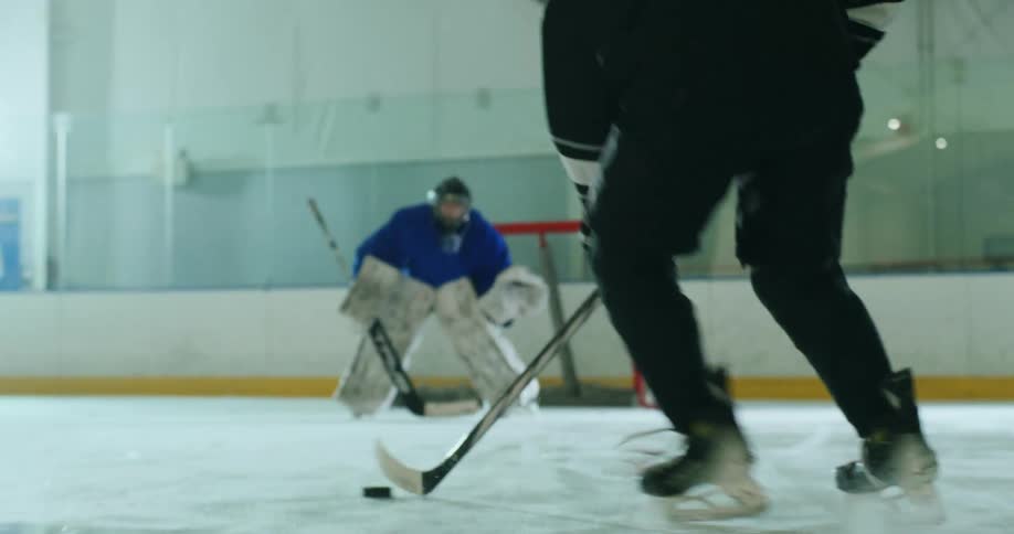 A player shoots a puck at a goalie on an ice hockey rink