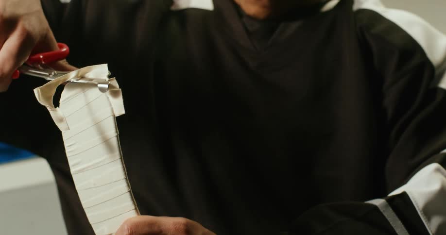 Closeup of a persons hands cutting a ribbon on a hockey stick