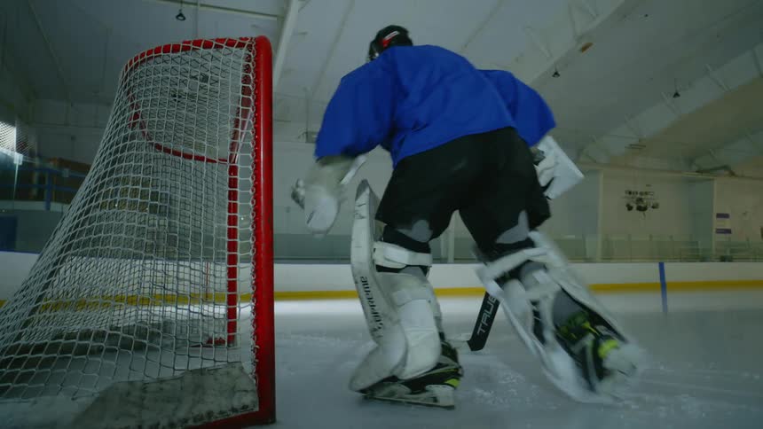 A goalie prepares for a game in front of a goal on an ice hockey rink