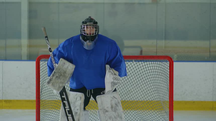 A man in hockey clothes puts on his helmet and stands in front of the goal