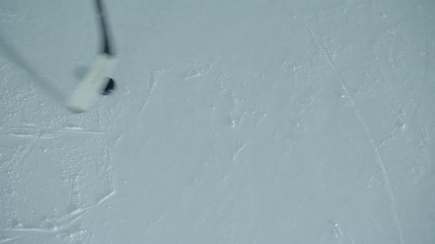A hockey stick moving a puck over an ice rink