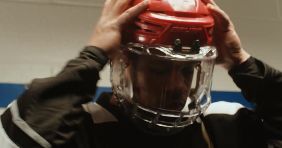 A teenager is putting on his hockey helmet