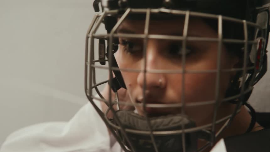 Portrait of a young woman putting on her protective hockey helmet