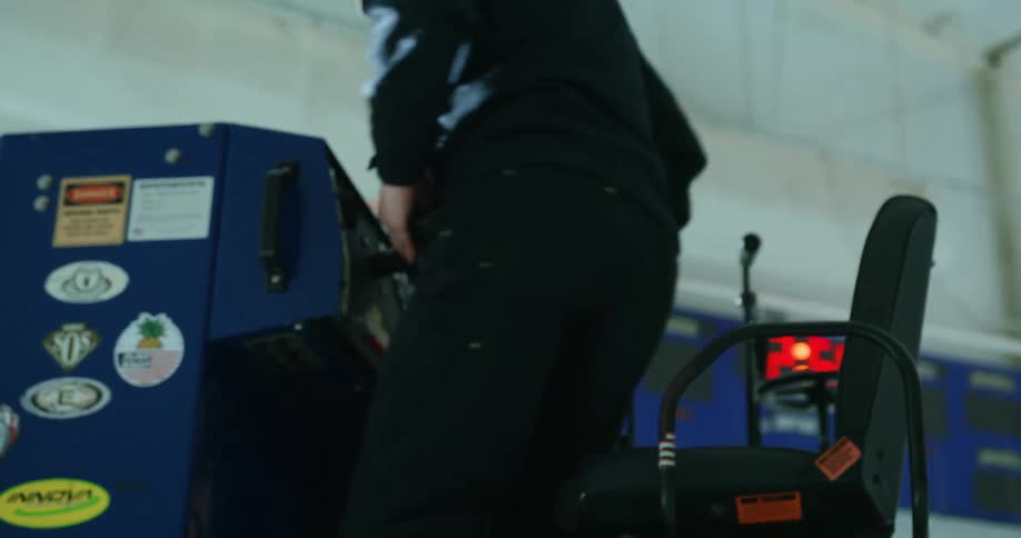 Man climbing onto a zamboni in an ice rink