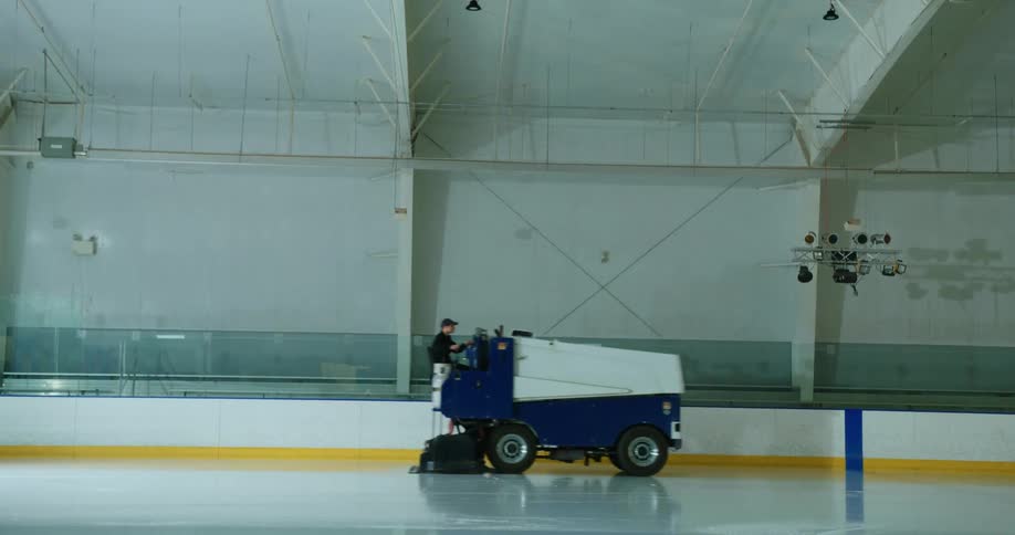 Man driving a zamboni near the edge of an ice rink