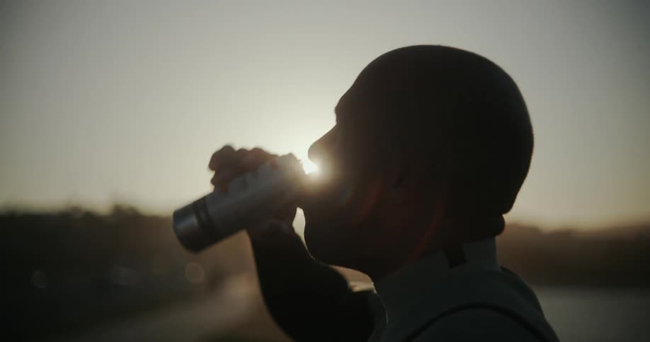 An athlete drinks an energy drink at sunset on the coast