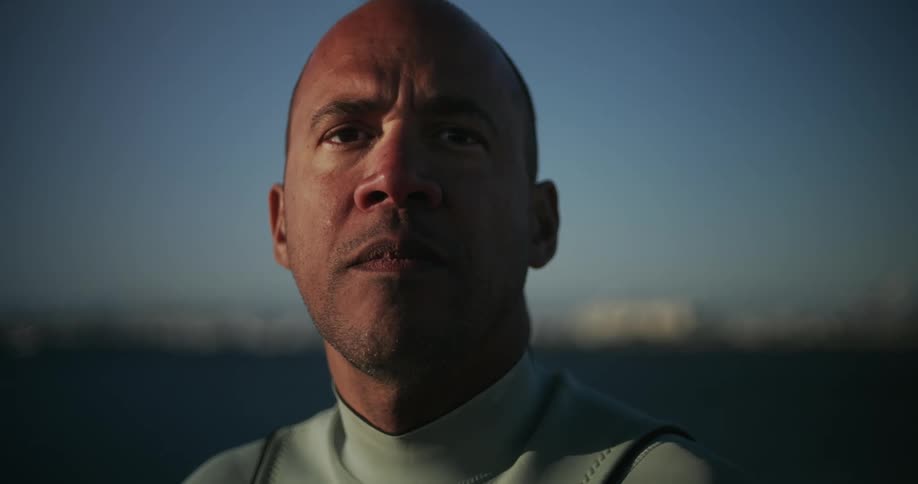 An athlete in a wetsuit watches the ocean beyond him