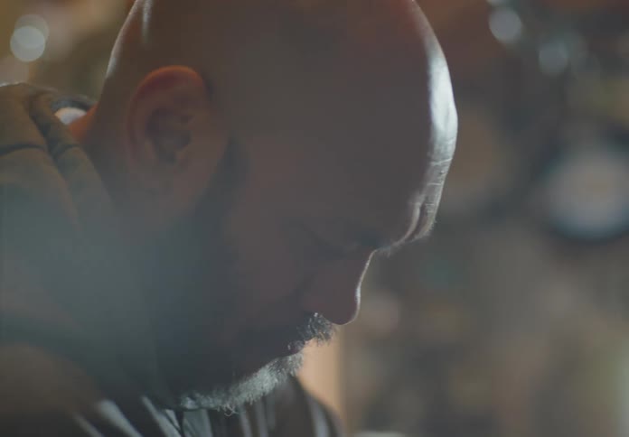 A bald, bearded man and dark-haired young woman concentrate as they work together to install a headlight on a motorcycle.