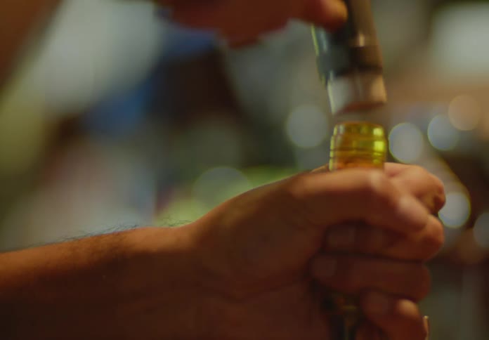 Close up of a male woodcarver's hands using a small hammer to tap a brass-topped chisel.